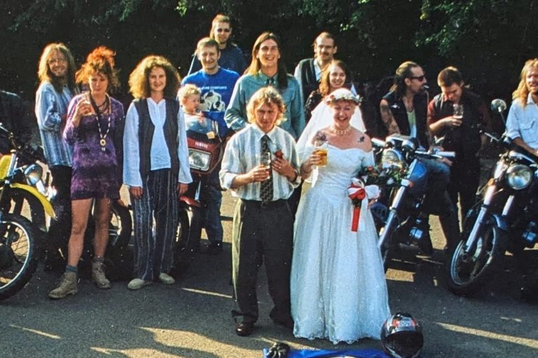 Male and female couple wearing wedding outfits with bikers and their motorbikes forming a circle around them.