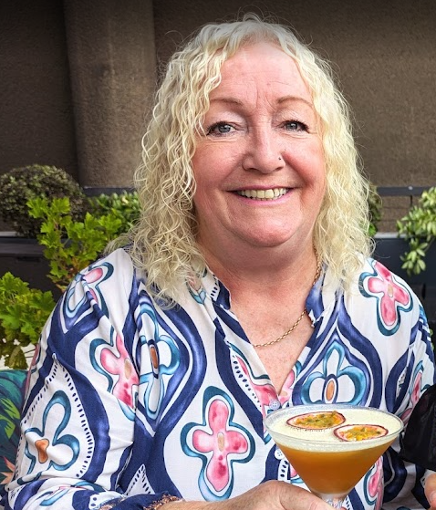 Woman with shoulder-length platinum-blonde curly hair and warm friendly smile.